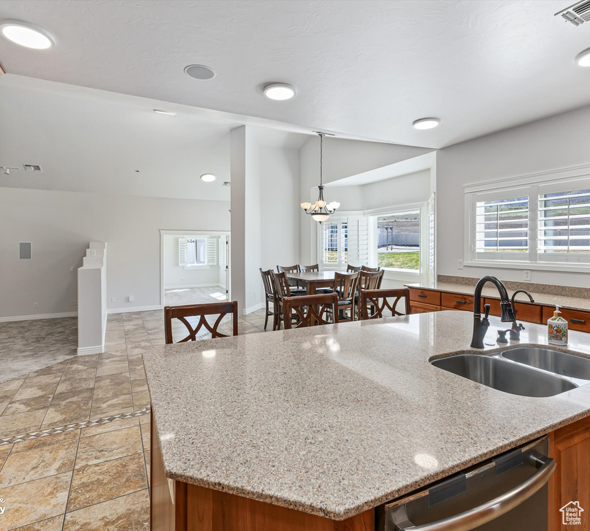 Kitchen with light stone counters, sink, pendant lighting, and a kitchen island with sink