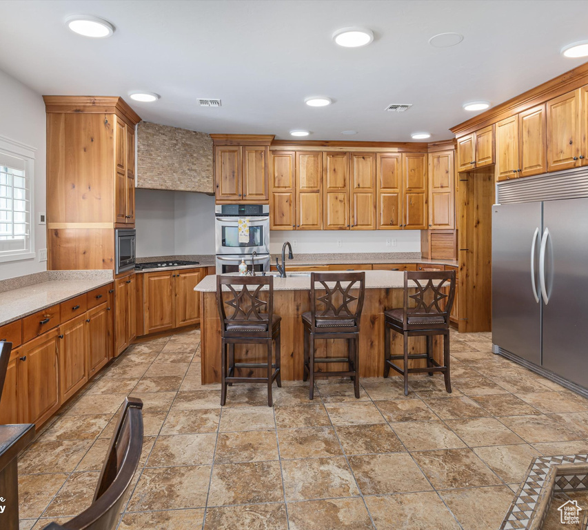 Kitchen featuring built in appliances, a breakfast bar area, light tile flooring, and a kitchen island with sink