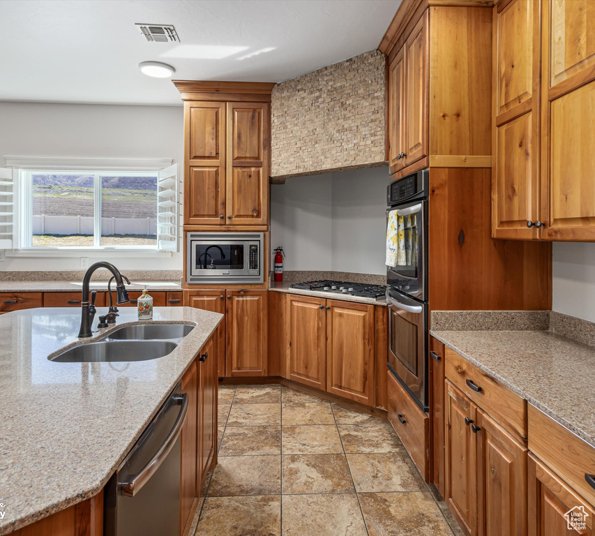 Kitchen with sink, stainless steel appliances, light tile floors, and light stone counters