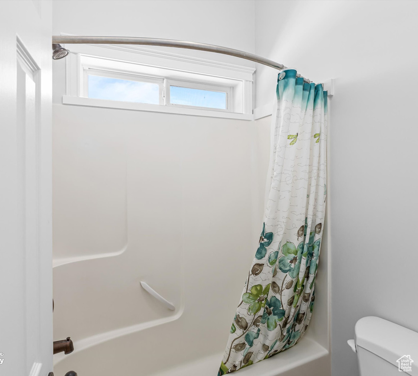 Bathroom with plenty of natural light, shower / bath combination with curtain, and toilet