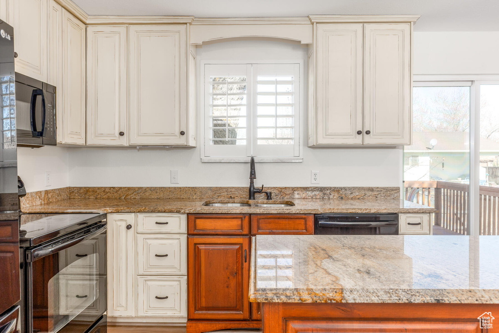 Kitchen featuring sink, cream cabinets, black appliances, and light stone countertops