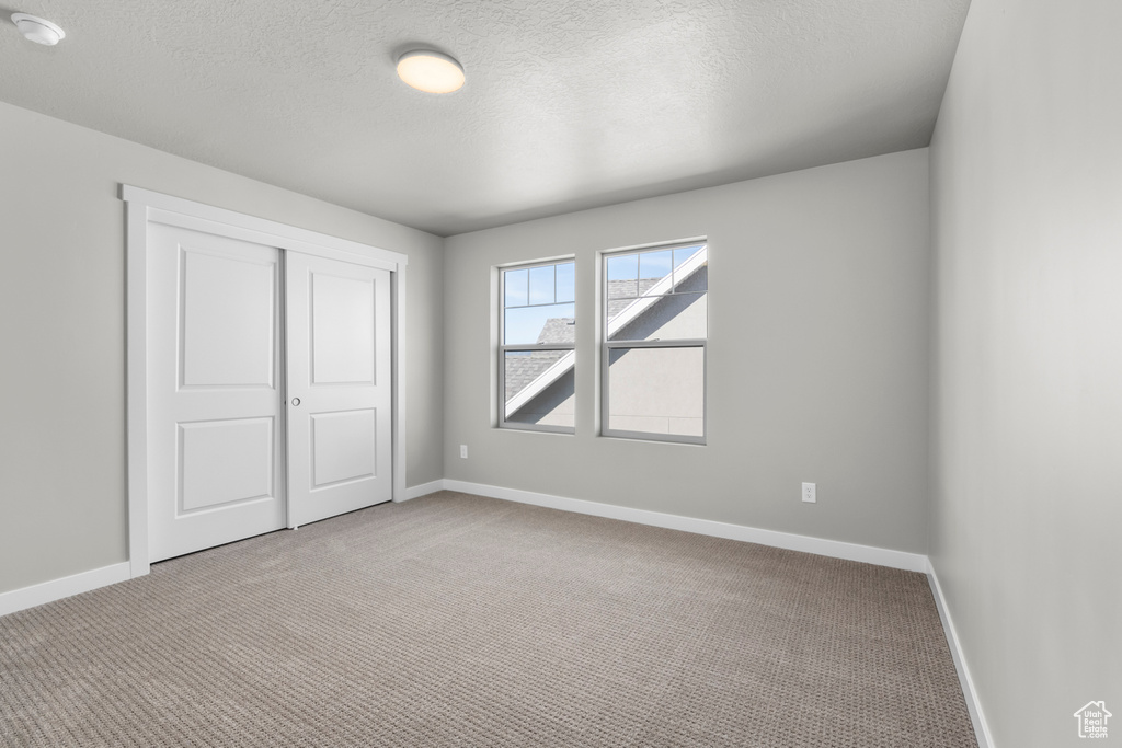 Unfurnished bedroom featuring light colored carpet, a closet, and a textured ceiling