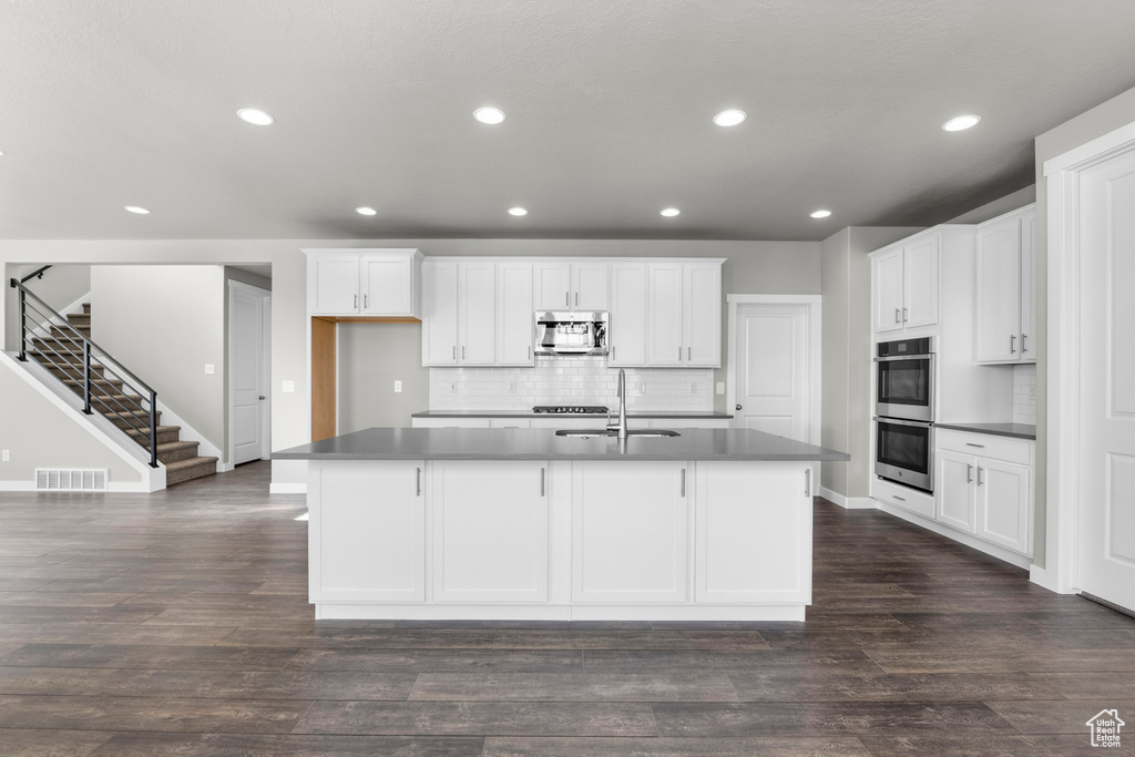 Kitchen with a center island with sink, white cabinetry, stainless steel appliances, and dark wood-type flooring