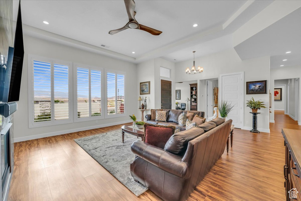 Living room featuring ceiling fan with notable chandelier, light hardwood / wood-style flooring, and a raised ceiling