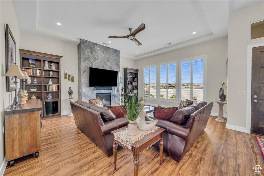 Living room featuring a fireplace, light hardwood / wood-style flooring, ceiling fan, and a tray ceiling