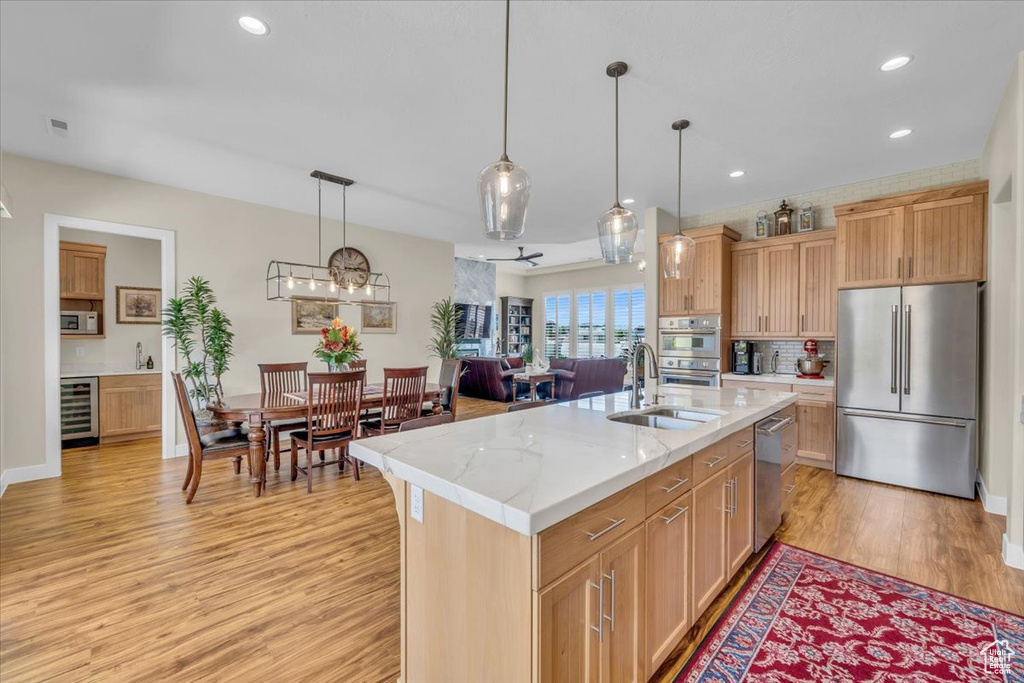 Kitchen with pendant lighting, a kitchen island with sink, light stone countertops, light hardwood / wood-style flooring, and appliances with stainless steel finishes