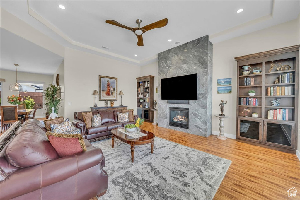 Living room with a fireplace, ceiling fan, a tray ceiling, and light wood-type flooring