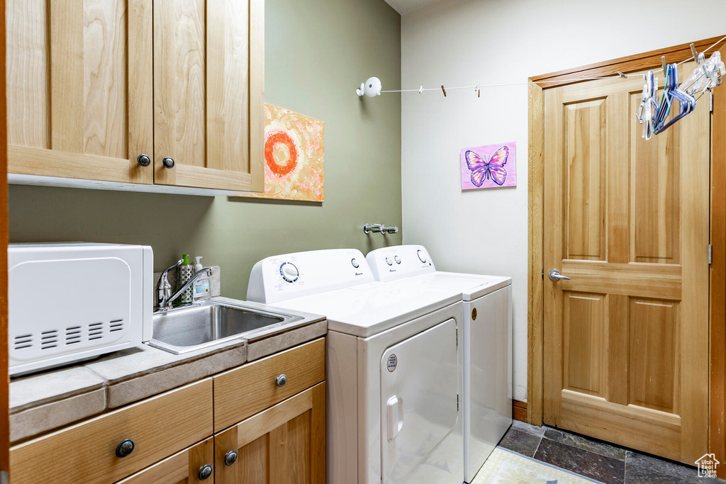 Clothes washing area with dark tile flooring, cabinets, sink, and washer and dryer