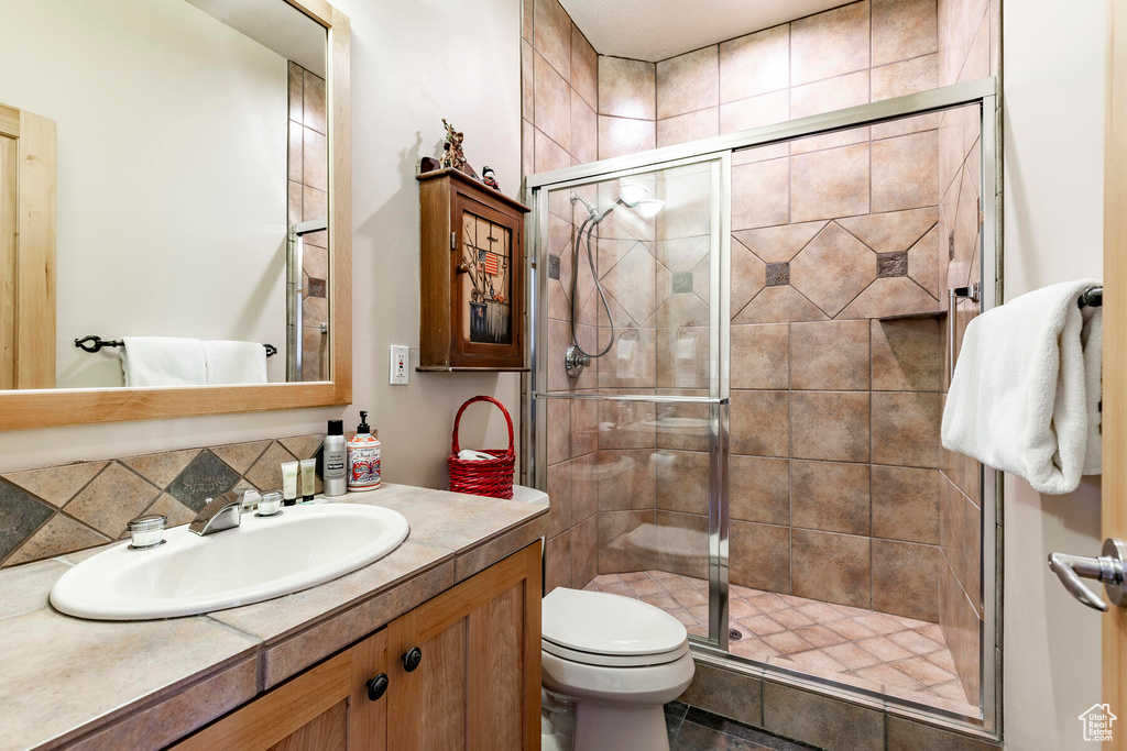 Bathroom with tile flooring, large vanity, backsplash, walk in shower, and toilet