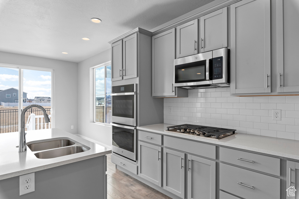 Kitchen featuring sink, light hardwood / wood-style floors, tasteful backsplash, gray cabinets, and stainless steel appliances