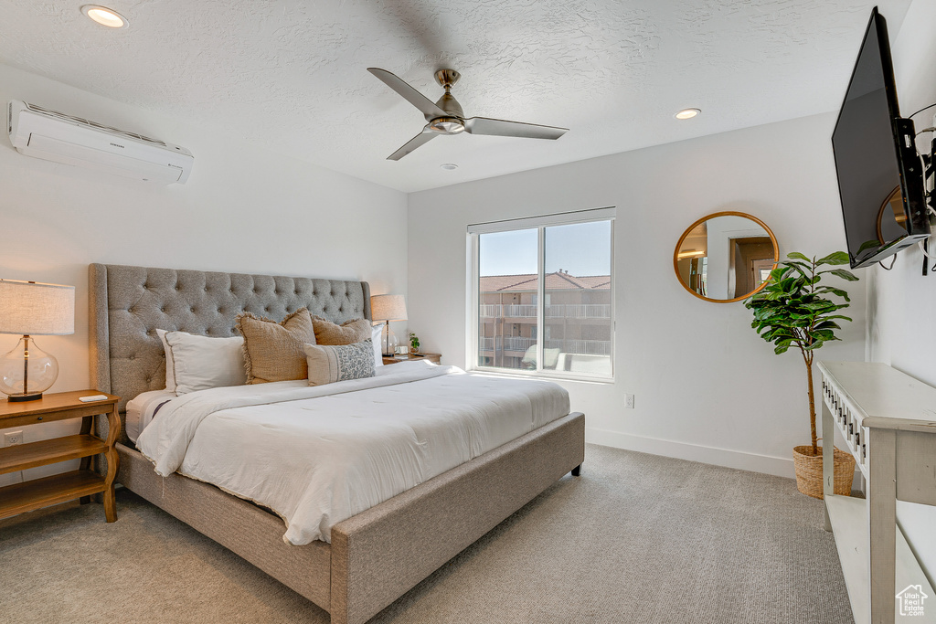 Carpeted bedroom with a textured ceiling, ceiling fan, and a wall mounted AC