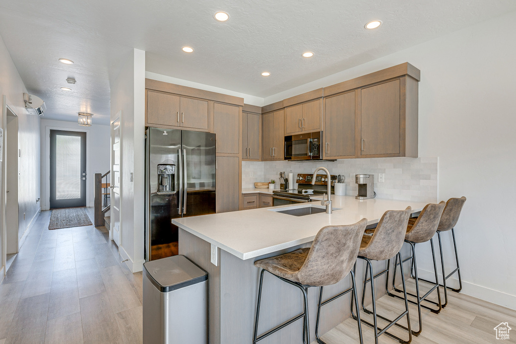 Kitchen featuring backsplash, light wood-type flooring, stainless steel appliances, and a breakfast bar