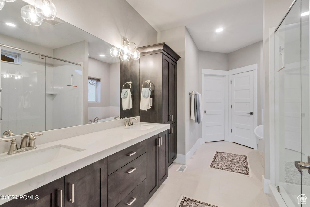 Bathroom featuring vanity with extensive cabinet space, double sink, tile flooring, and a shower with door
