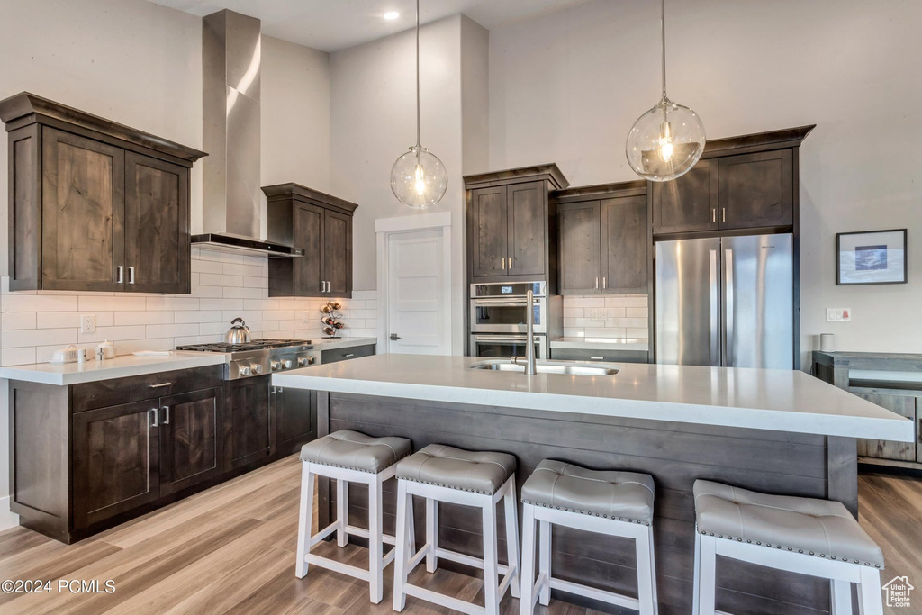 Kitchen featuring wall chimney exhaust hood, a towering ceiling, backsplash, stainless steel appliances, and pendant lighting