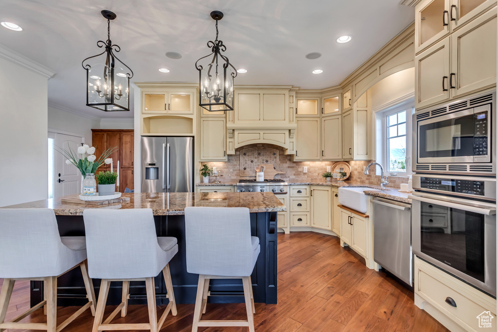 Kitchen featuring appliances with stainless steel finishes, a center island, sink, backsplash, and pendant lighting