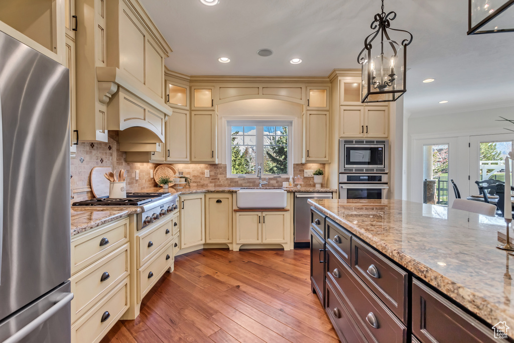Kitchen featuring pendant lighting, backsplash, appliances with stainless steel finishes, sink, and light hardwood / wood-style floors