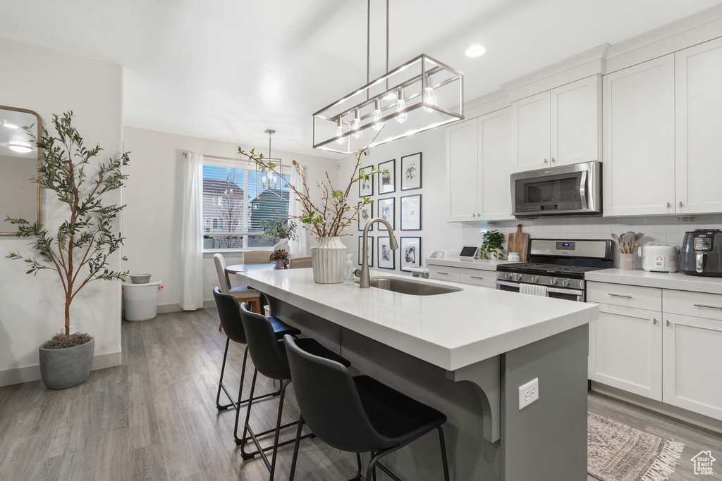 Kitchen featuring stainless steel appliances, light hardwood / wood-style floors, an island with sink, white cabinetry, and sink