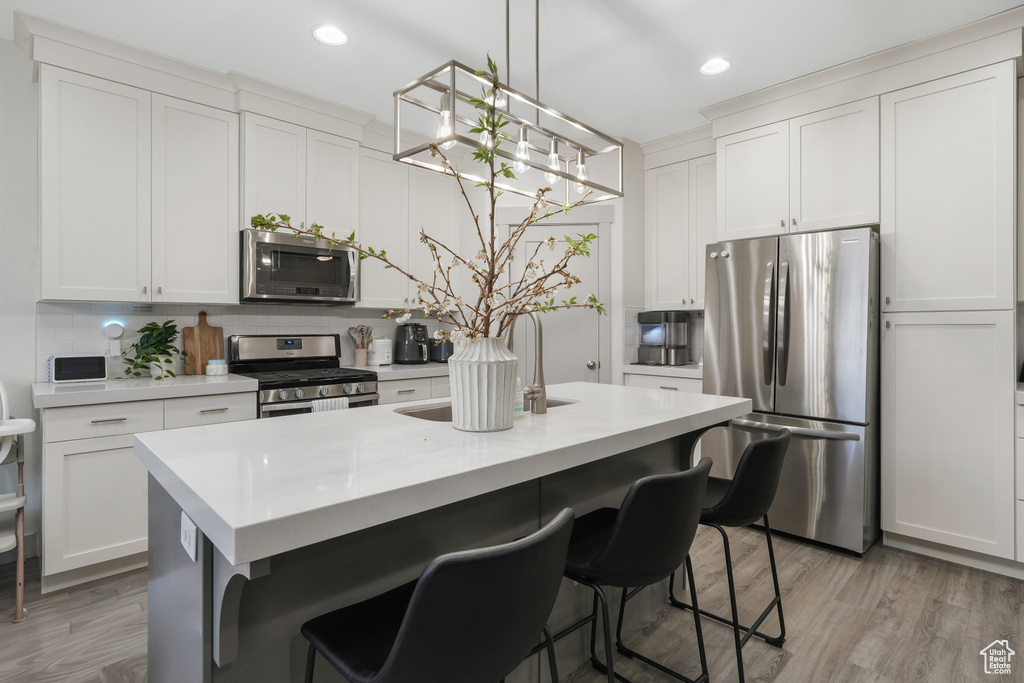 Kitchen featuring stainless steel appliances, white cabinetry, a breakfast bar area, and light wood-type flooring