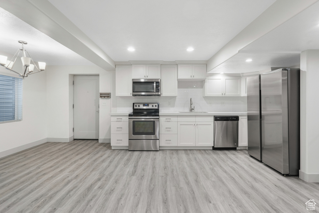 Kitchen featuring hanging light fixtures, white cabinets, stainless steel appliances, a notable chandelier, and light hardwood / wood-style floors