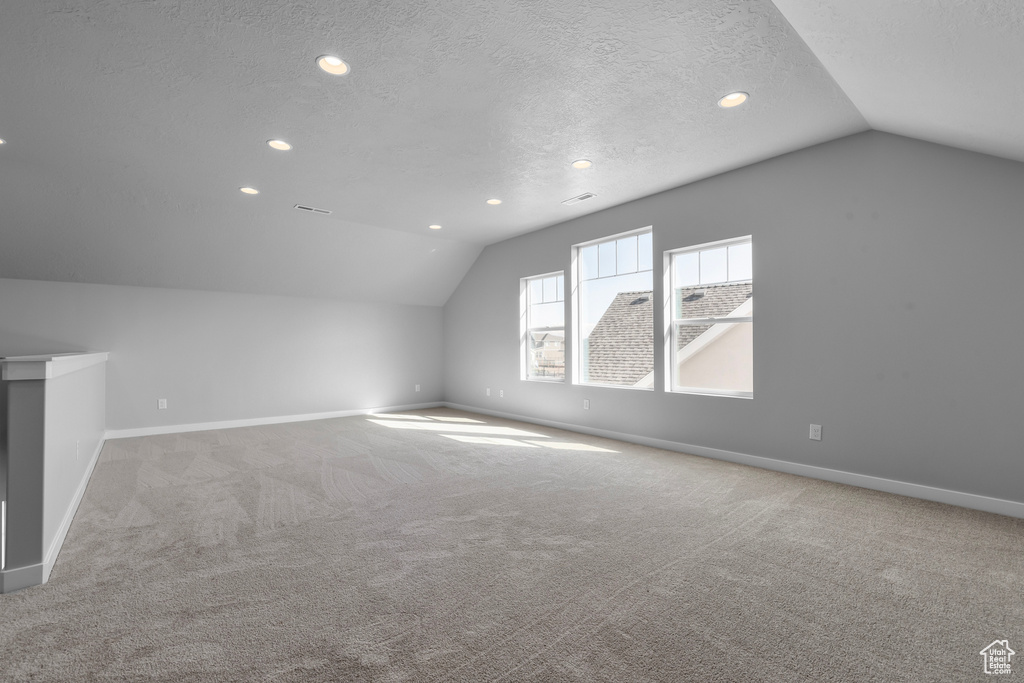 Bonus room with light colored carpet, lofted ceiling, and a textured ceiling