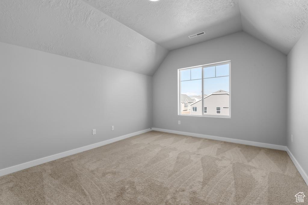 Bonus room with a textured ceiling, light carpet, and lofted ceiling