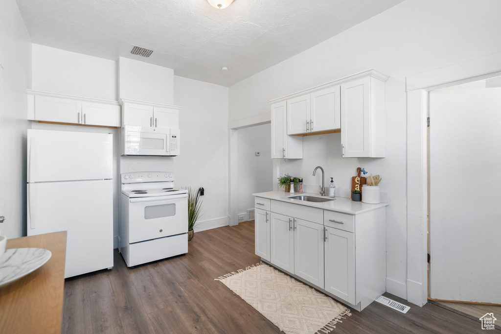 Kitchen with white appliances, dark wood-type flooring, sink, and white cabinetry
