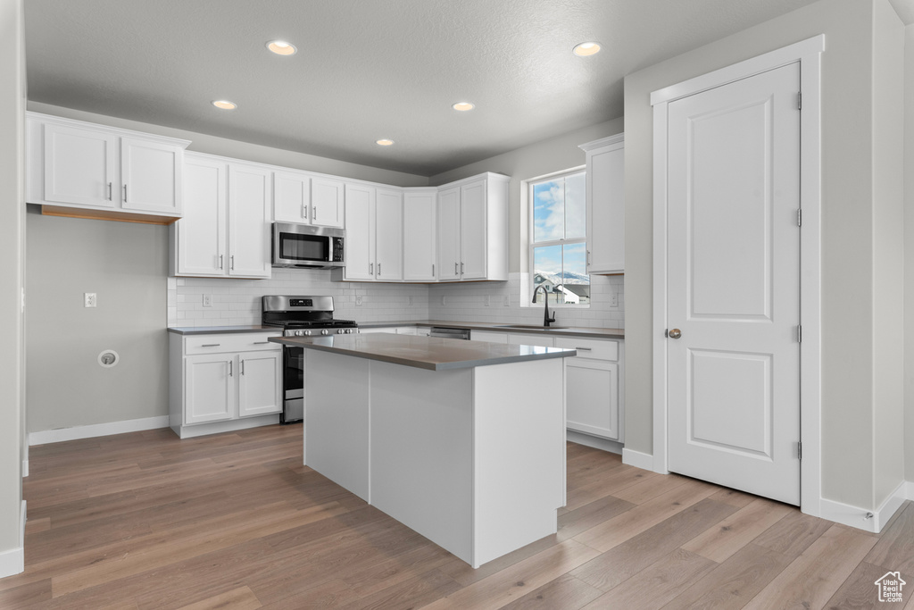 Kitchen with light hardwood / wood-style flooring, a center island, white cabinetry, and stainless steel appliances