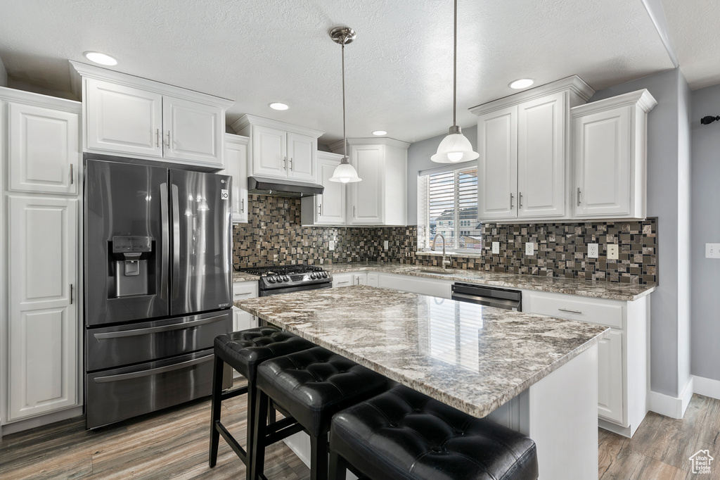 Kitchen featuring a center island, light hardwood / wood-style flooring, white cabinetry, appliances with stainless steel finishes, and a kitchen bar