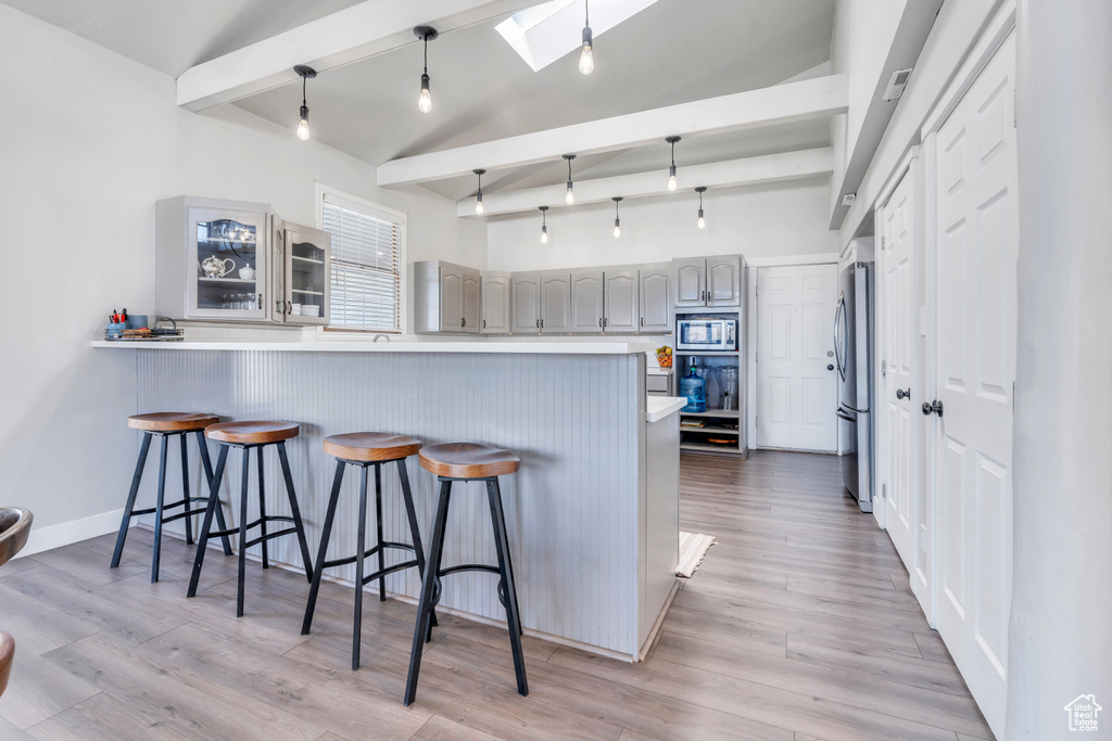 Kitchen with gray cabinets, light hardwood / wood-style flooring, lofted ceiling with skylight, kitchen peninsula, and stainless steel appliances