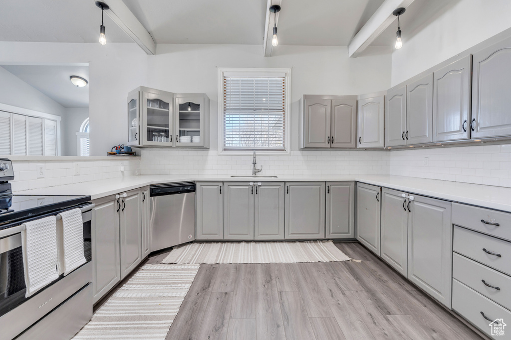 Kitchen with backsplash, gray cabinets, stainless steel appliances, pendant lighting, and light wood-type flooring