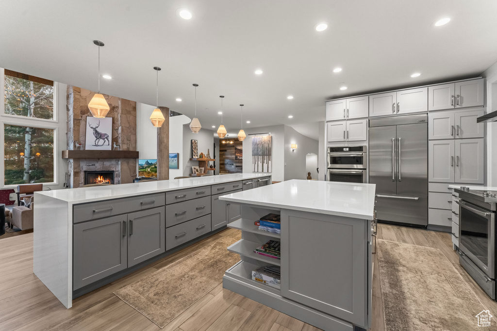 Kitchen featuring a center island, gray cabinetry, appliances with stainless steel finishes, and a fireplace