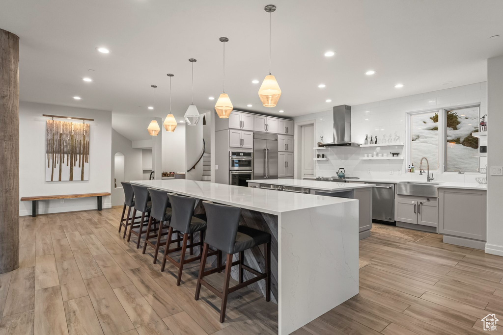 Kitchen featuring decorative light fixtures, a kitchen island, stainless steel appliances, wall chimney range hood, and a breakfast bar