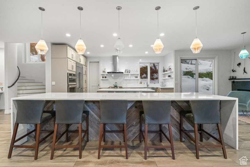 Kitchen with light hardwood / wood-style floors, wall chimney range hood, backsplash, a breakfast bar area, and hanging light fixtures