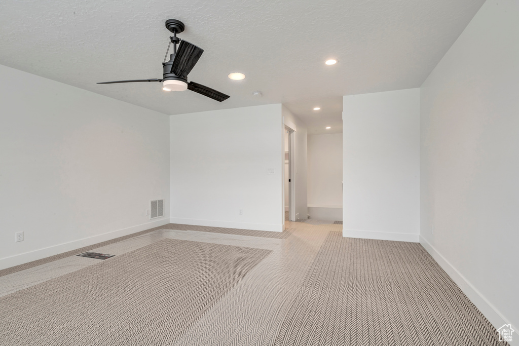 Spare room featuring light colored carpet, ceiling fan, and a textured ceiling