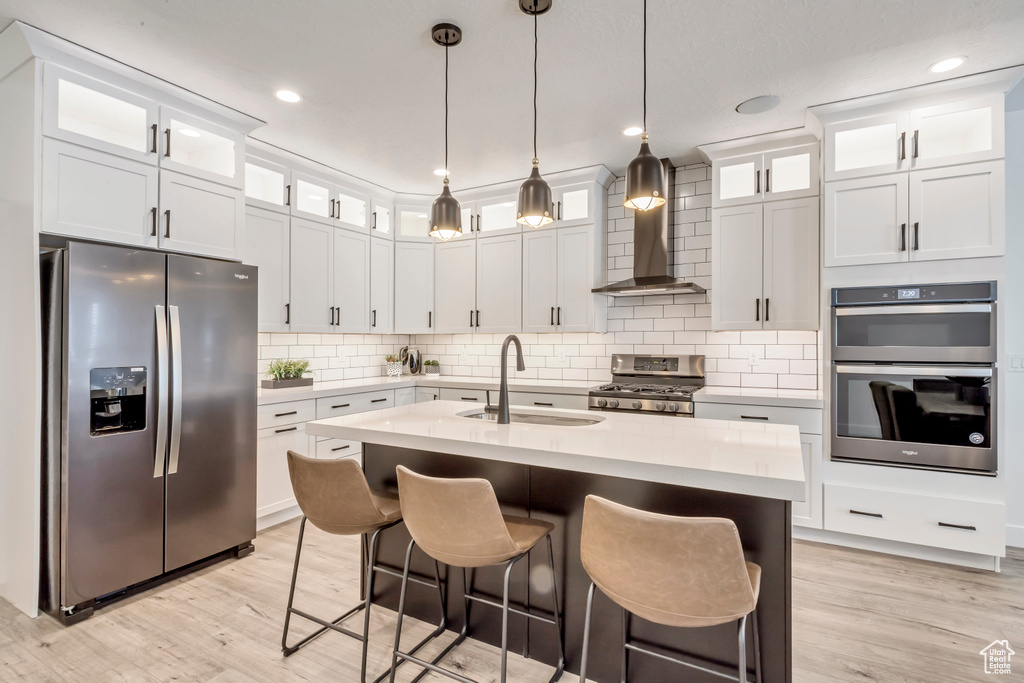 Kitchen with hanging light fixtures, light hardwood / wood-style flooring, appliances with stainless steel finishes, sink, and a center island with sink