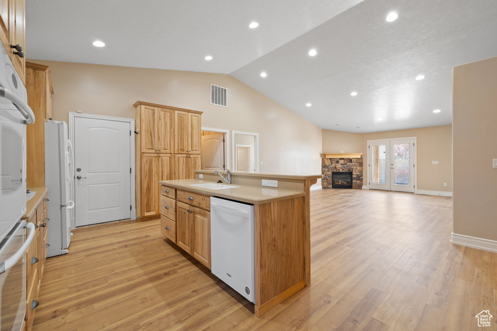 Kitchen with light hardwood / wood-style floors, an island with sink, a fireplace, white appliances, and sink