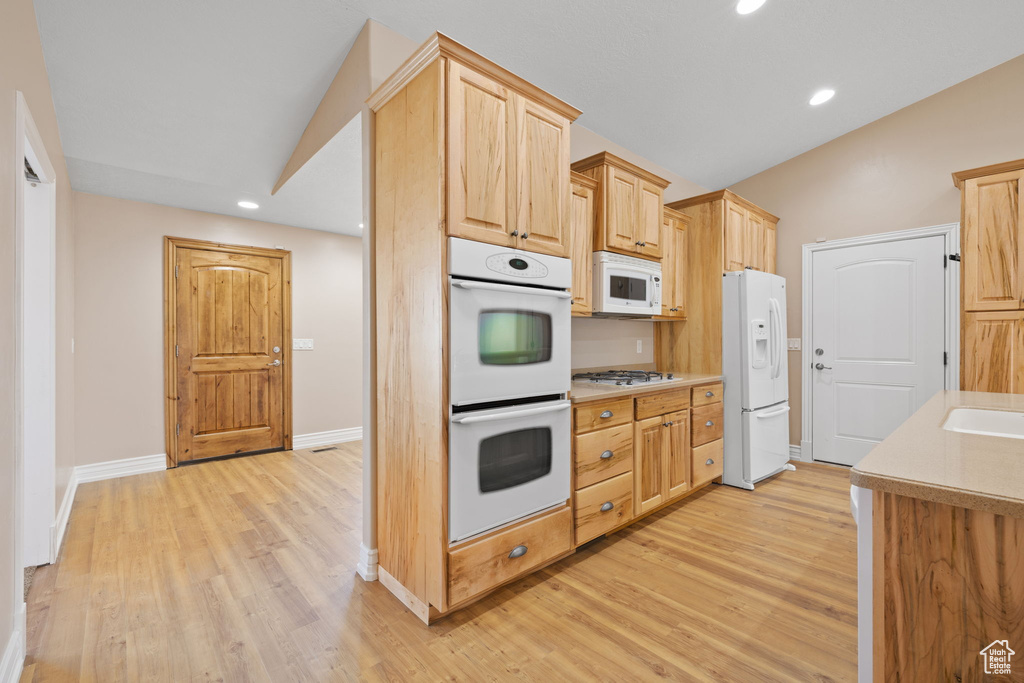 Kitchen with light brown cabinets, lofted ceiling, white appliances, and light hardwood / wood-style floors