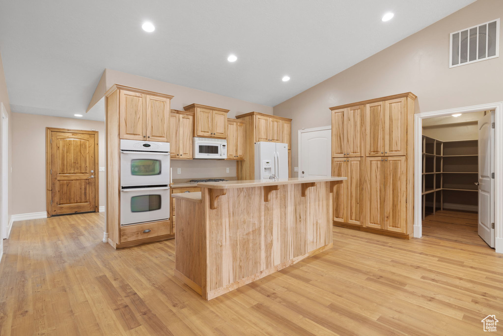 Kitchen with a center island, light brown cabinets, light hardwood / wood-style floors, lofted ceiling, and white appliances