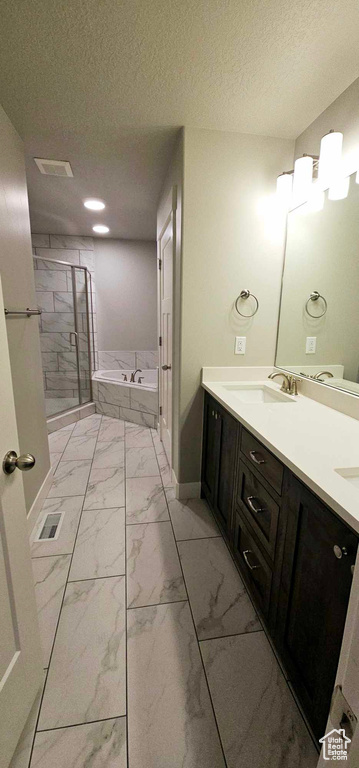 Bathroom with a textured ceiling, vanity with extensive cabinet space, shower with separate bathtub, and tile flooring
