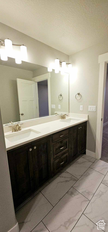 Bathroom with dual bowl vanity, tile floors, and a textured ceiling