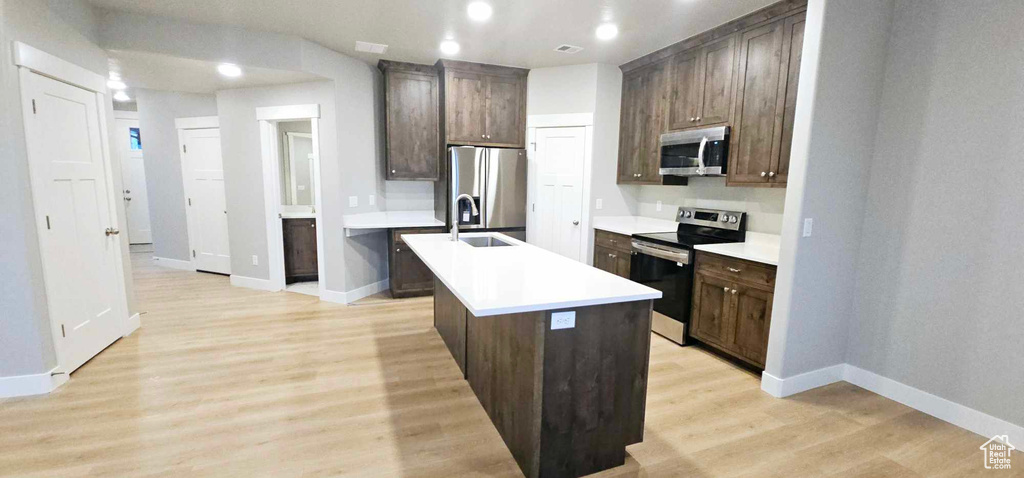 Kitchen with dark brown cabinets, light hardwood / wood-style flooring, a kitchen island with sink, and appliances with stainless steel finishes