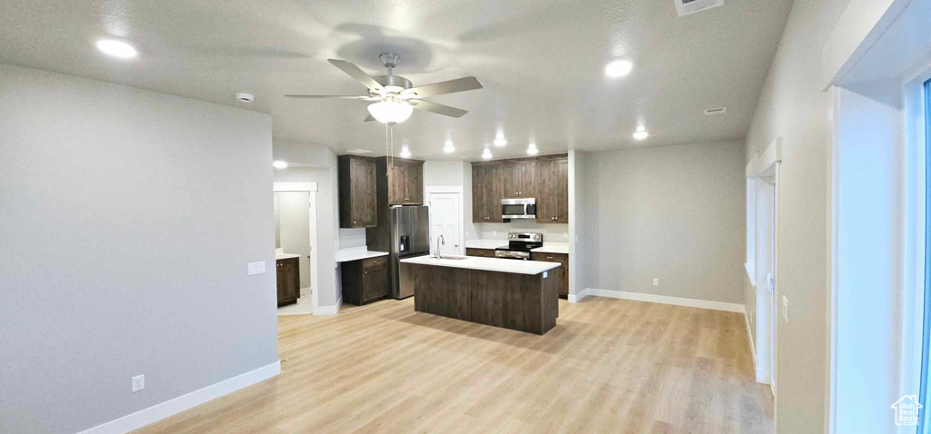 Kitchen with appliances with stainless steel finishes, light hardwood / wood-style flooring, ceiling fan, and a kitchen island with sink