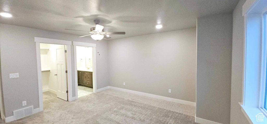 Unfurnished bedroom featuring light carpet, ceiling fan, and ensuite bathroom