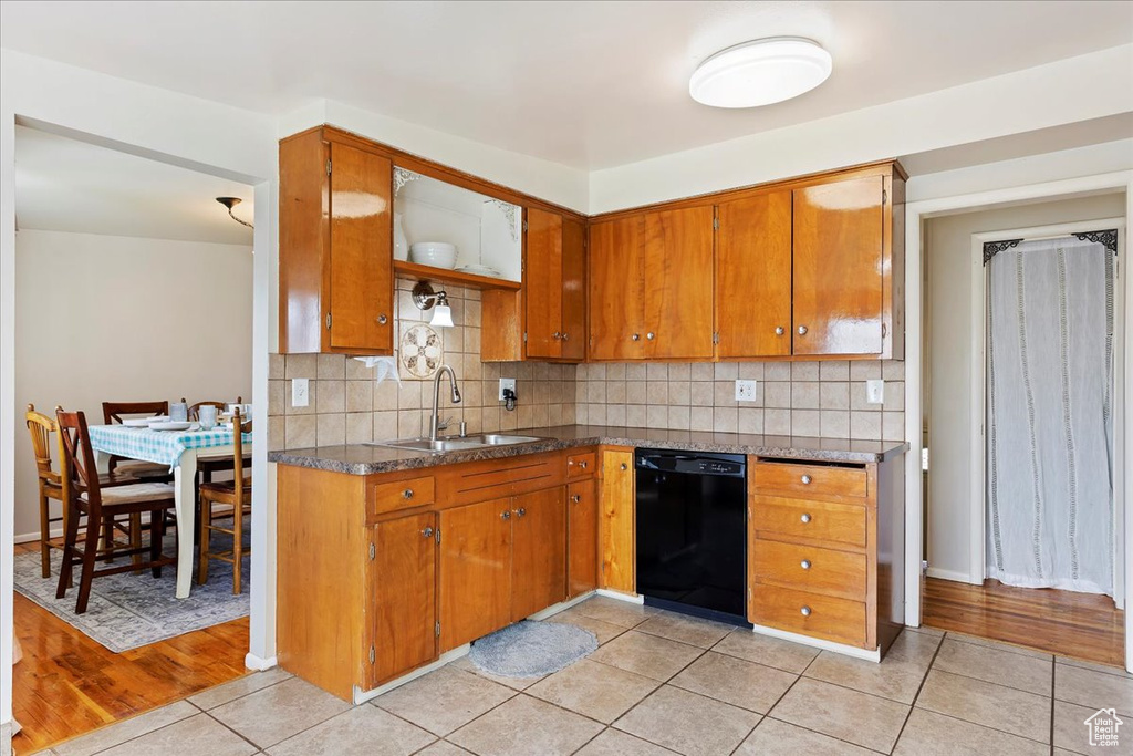 Kitchen featuring backsplash, sink, light wood-type flooring, and black dishwasher
