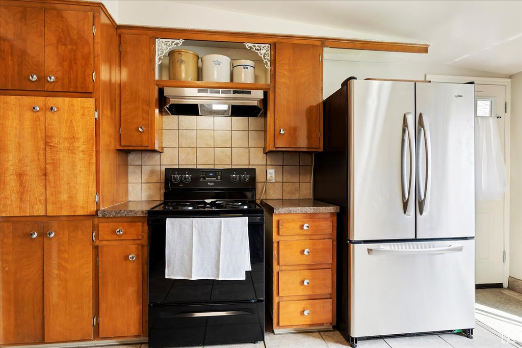 Kitchen with ventilation hood, light tile flooring, black / electric stove, tasteful backsplash, and stainless steel fridge