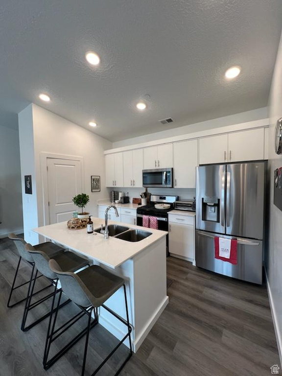 Kitchen with white cabinets, dark hardwood / wood-style flooring, stainless steel appliances, sink, and a breakfast bar area