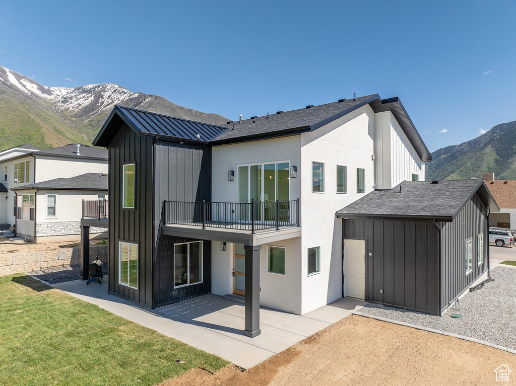 Rear view of house with a mountain view, a lawn, a balcony, and a patio