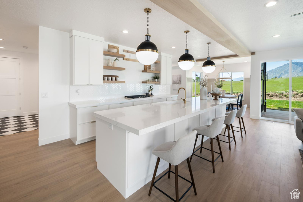 Kitchen with tasteful backsplash, white cabinetry, an island with sink, light wood-type flooring, and pendant lighting