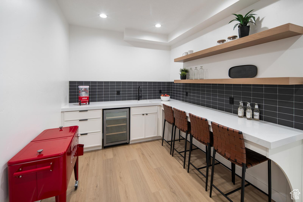 Kitchen featuring beverage cooler, light hardwood / wood-style flooring, backsplash, sink, and white cabinets