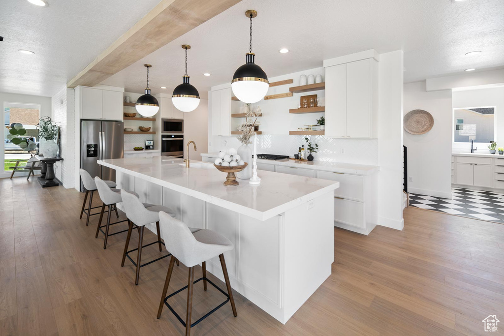 Kitchen with white cabinetry, a spacious island, light hardwood / wood-style flooring, stainless steel appliances, and pendant lighting